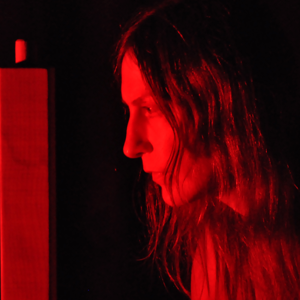 Side profile of a person with long hair illuminated by red light against a dark background.