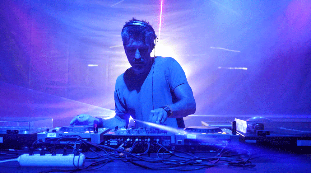 DJ wearing headphones mixing music on a console with blue and purple stage lighting.