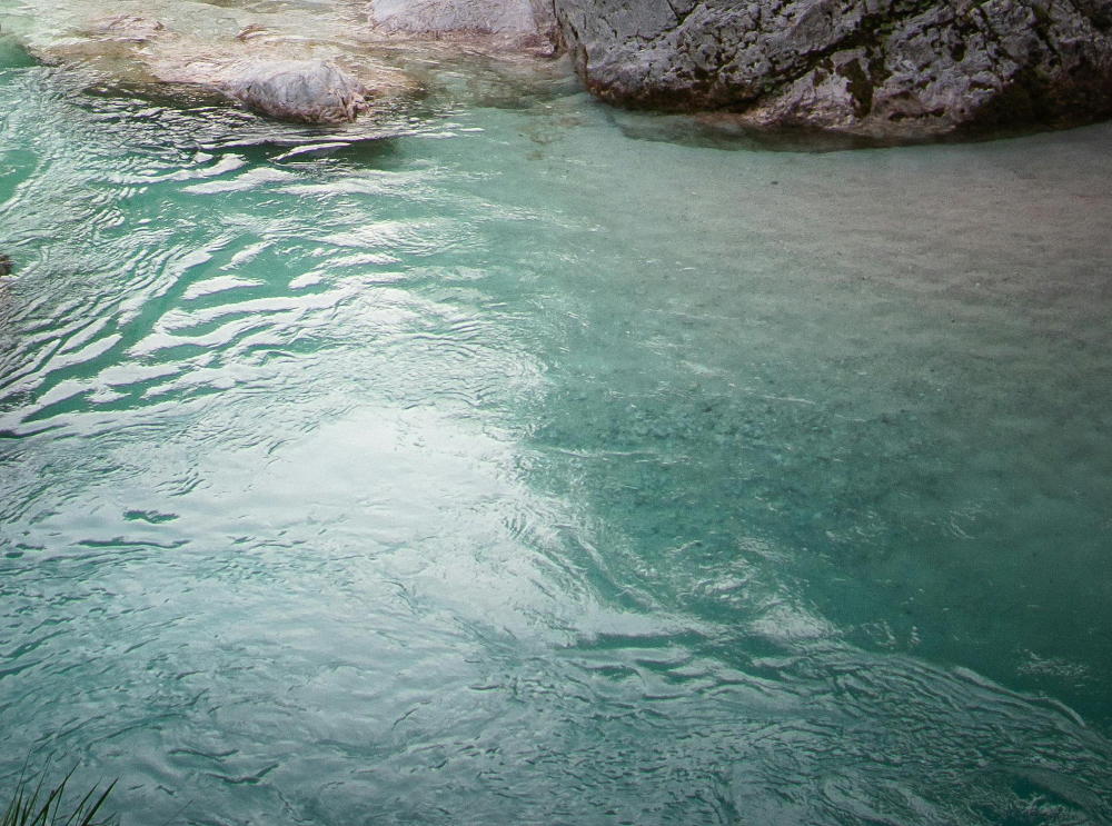 Clear turquoise river water flowing gently around grey rocky formations.