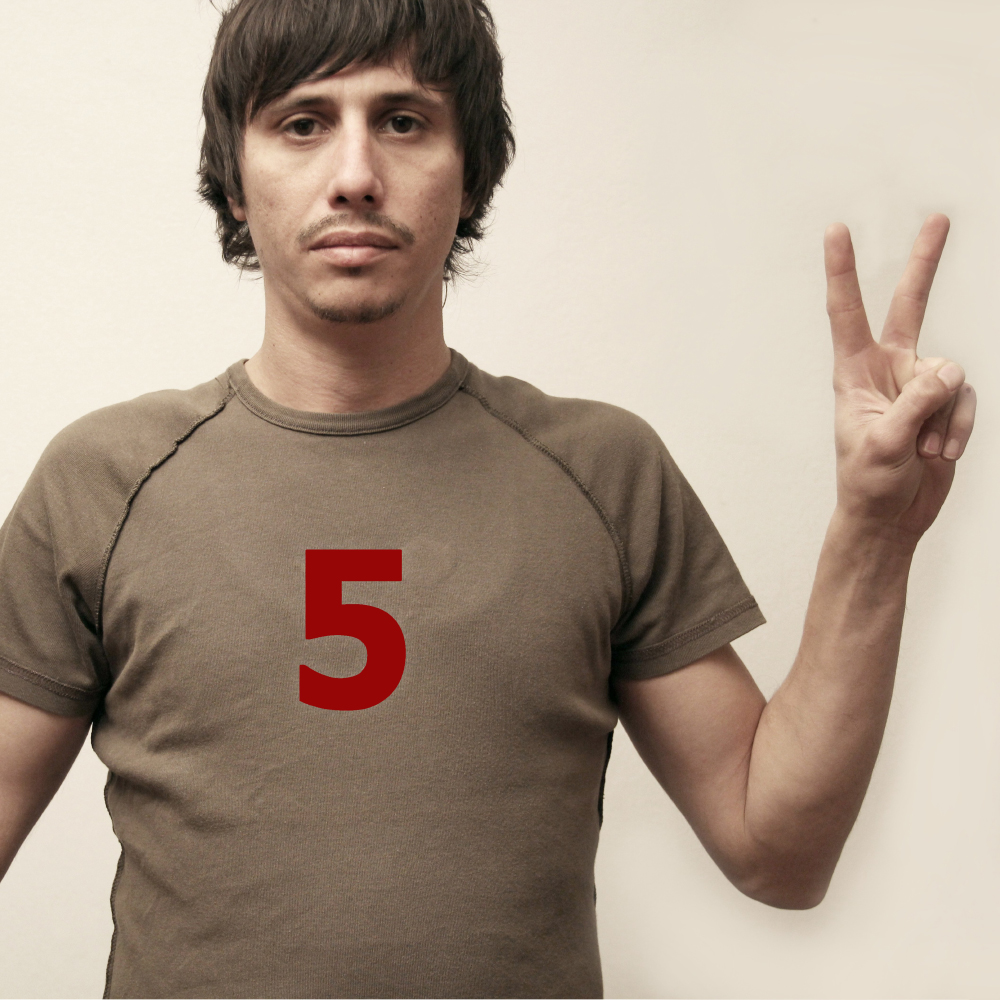 Man in a brown t-shirt showing two fingers raised, with a red number 5 on his shirt.