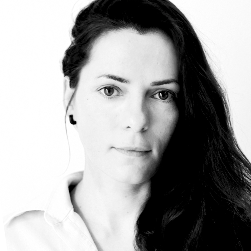 Black and white close-up portrait of a woman with long dark hair and a neutral expression, wearing a light-colored collared shirt.